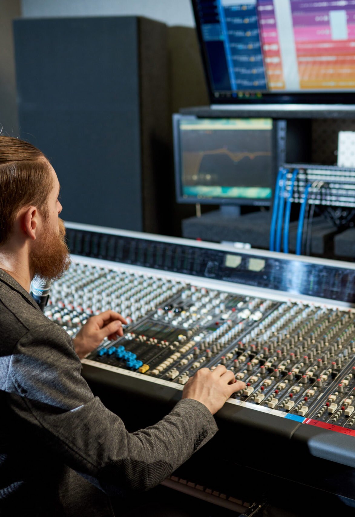 Stylish sound producer sitting at console and looking at monitors making up modern music.