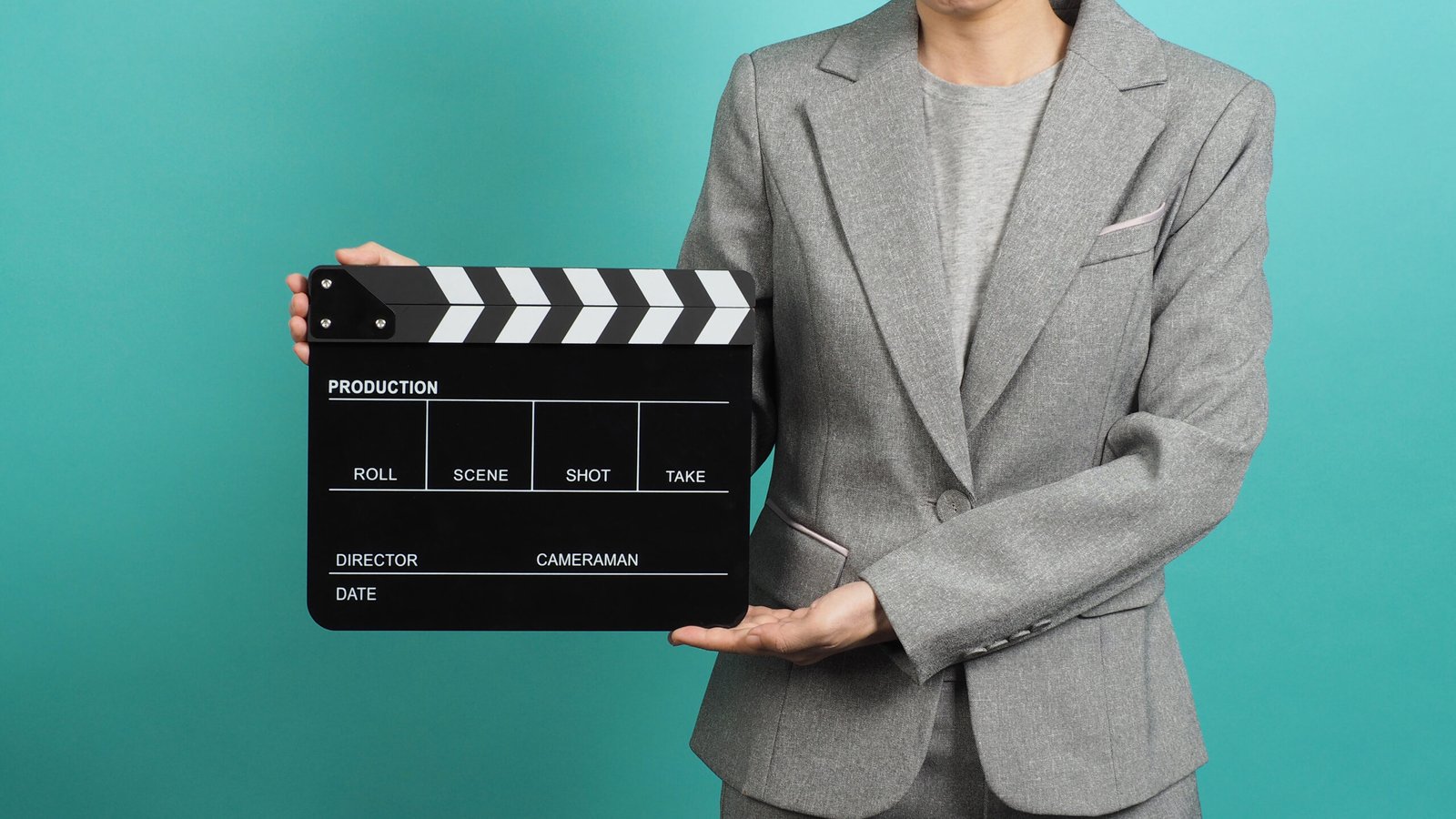 Woman hands holding black Clapperboard or film slate and wear grey suit. it use in videography ,movies and cinema industry on green or Tiffany Blue background.Clapper board for director.
